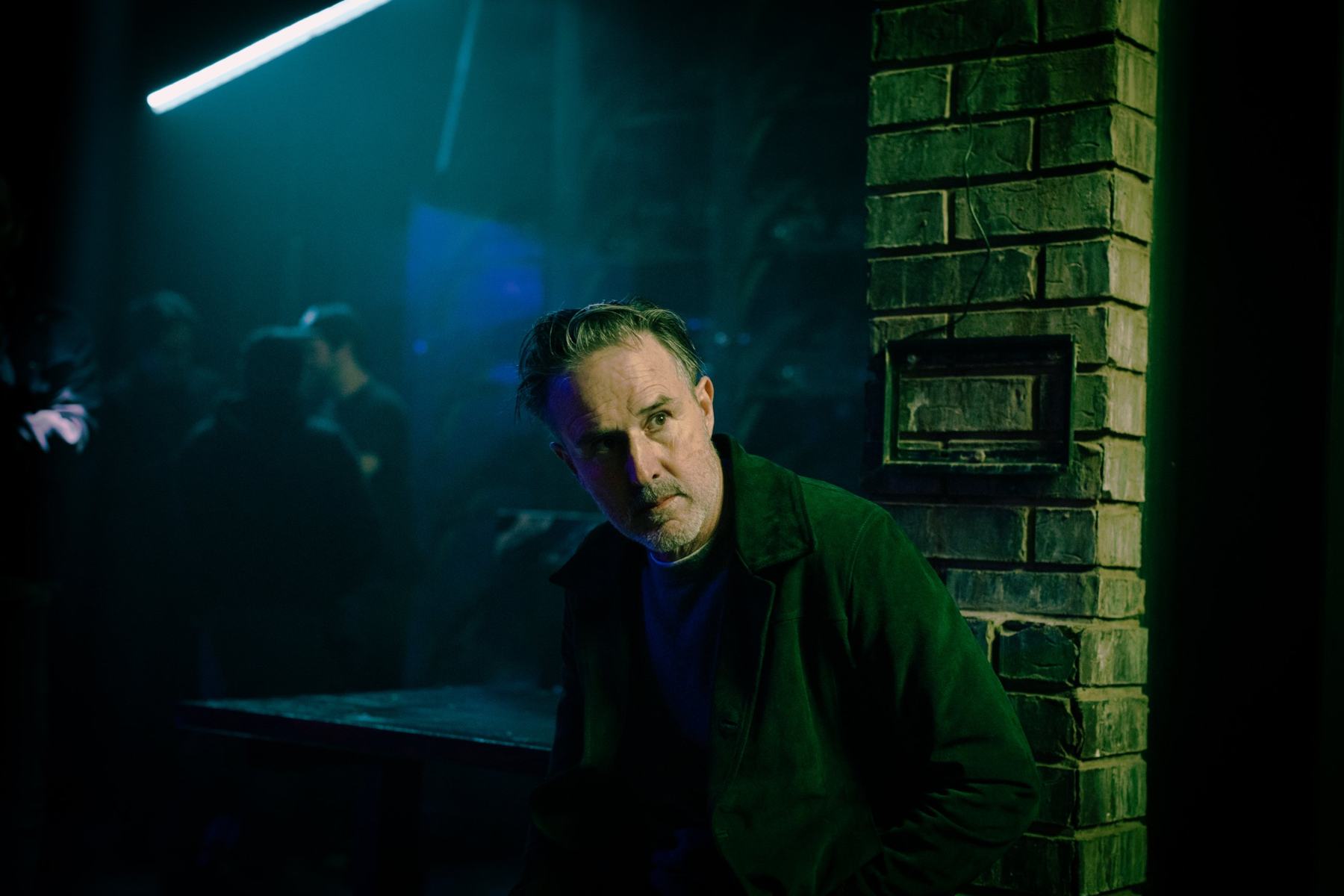 A man in a green jacket in a smoky, neon-lit club