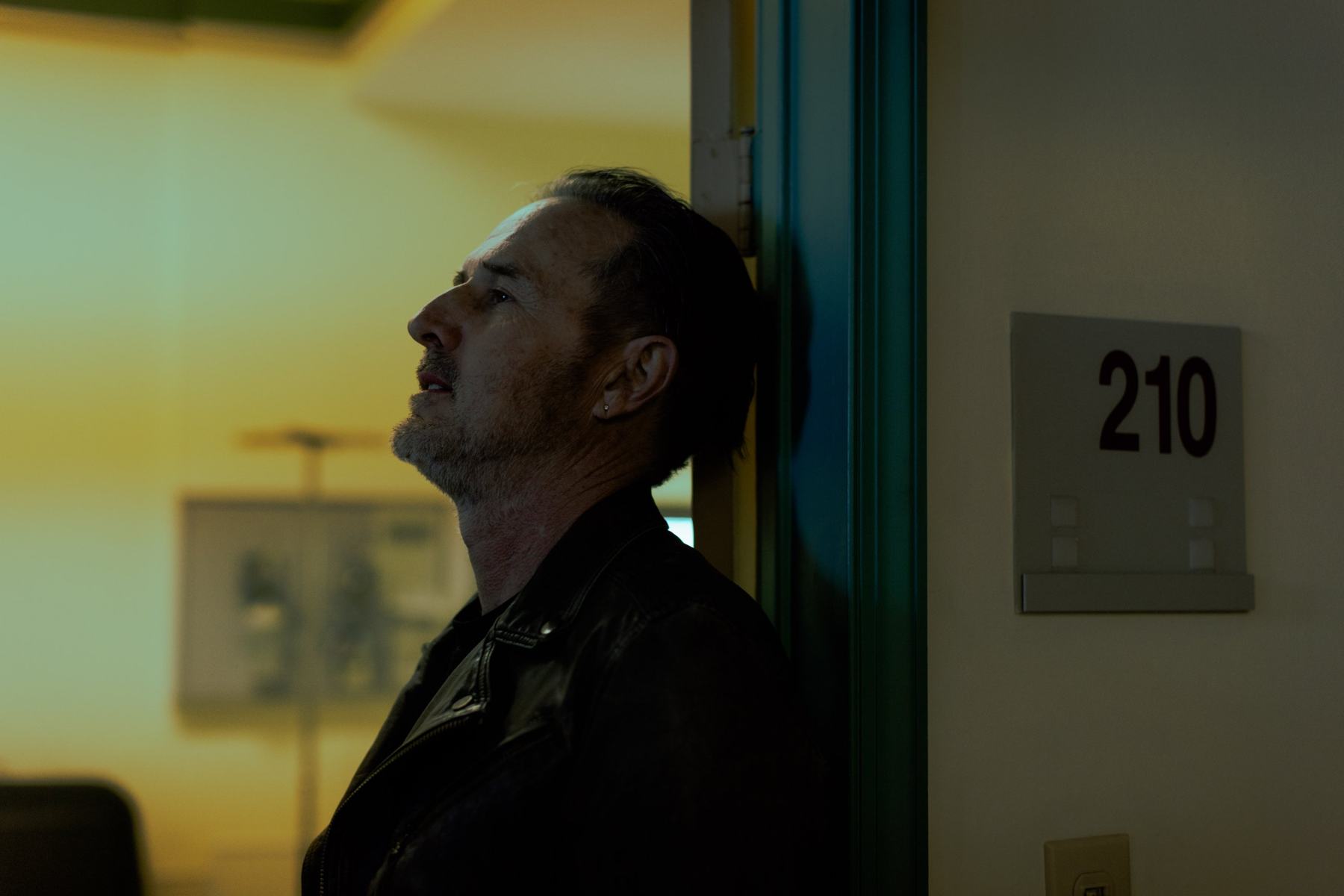 A man leaning against a hospital doorway, room 210